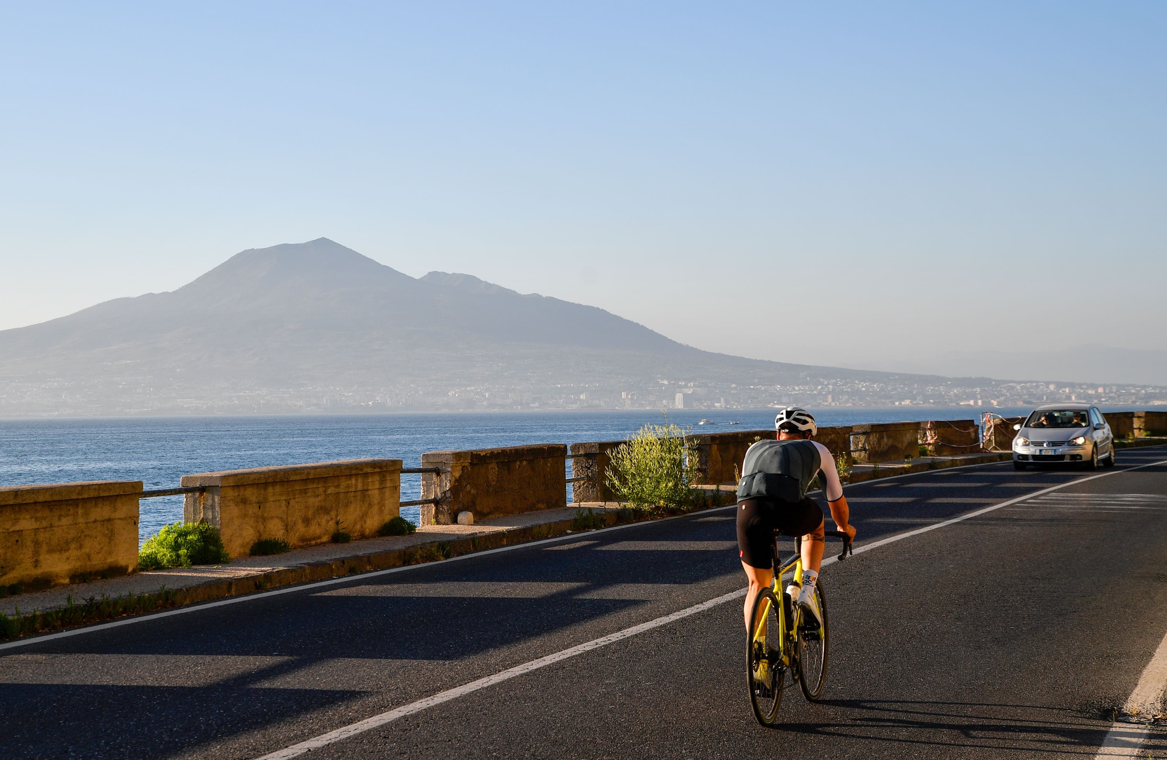 Cycliste chargé sur une route littorale, relief au fond